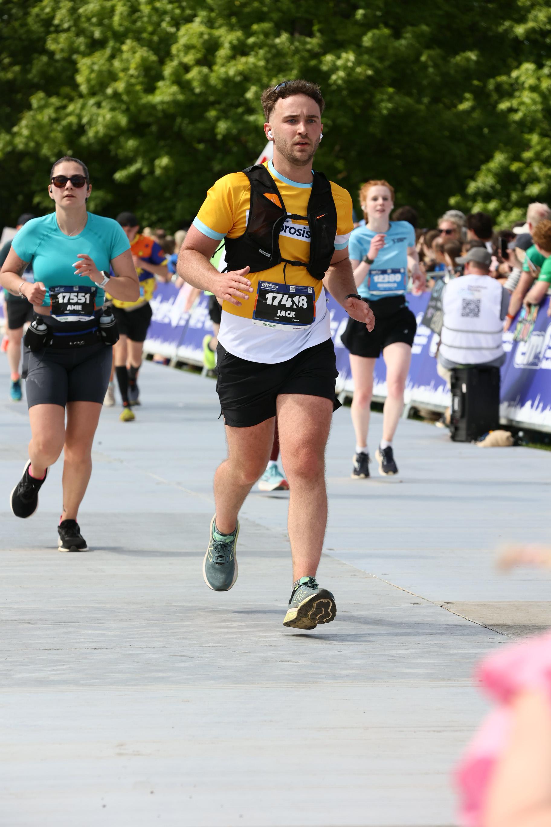 A man running in a marathon, wearing a yellow Cystic Fibrosis Trust vest