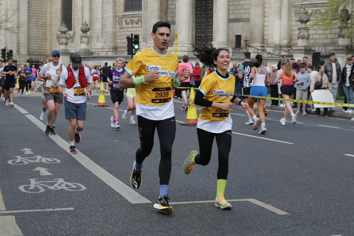 a man and woman running over the streets of London in a yellow cystic fibrosis trust top