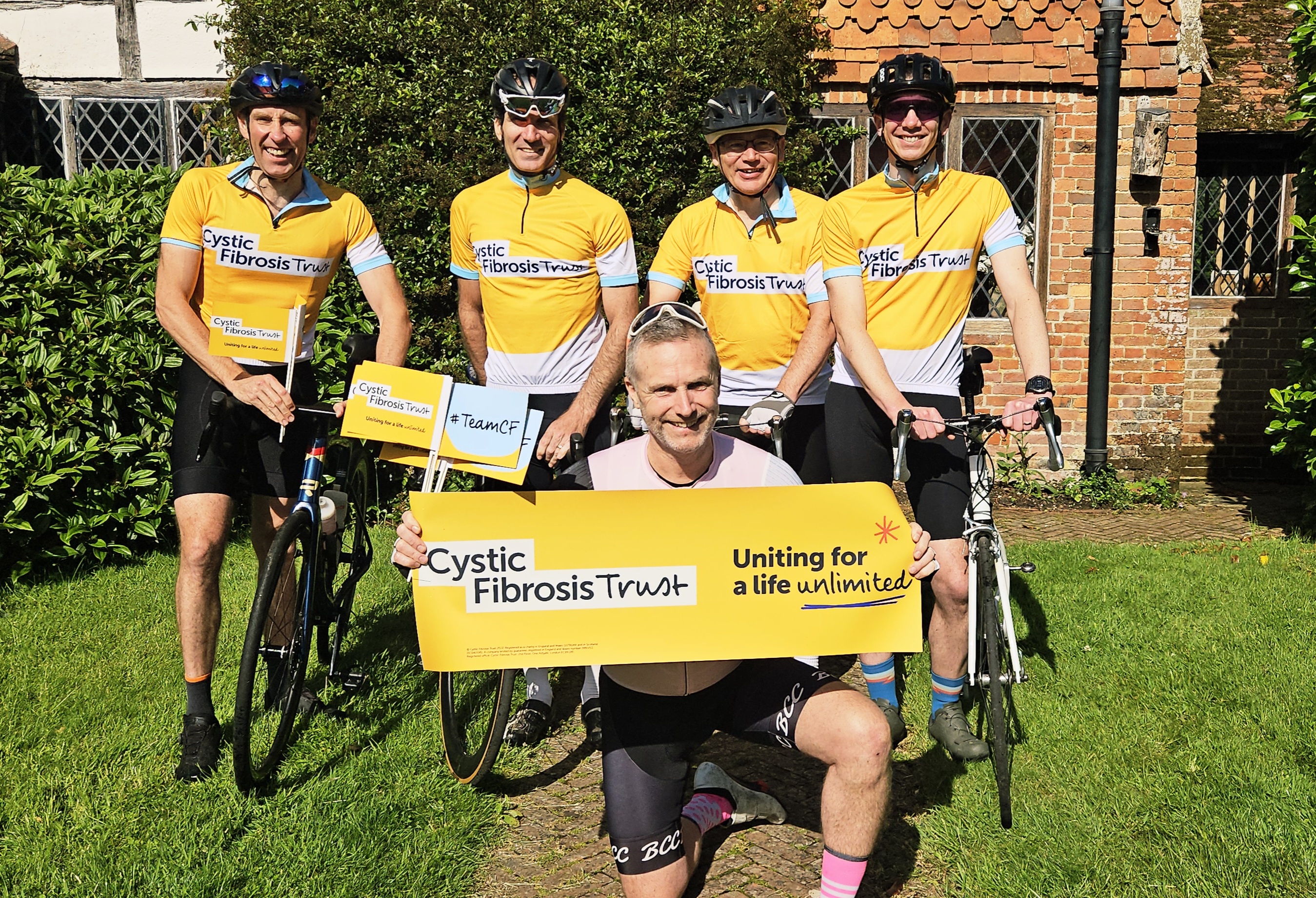 a group of 5 cyclists wearing yellow cystic fibrosis tops holding banners