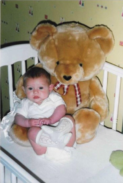 Annabelle as a baby, sat in a cot with a teddy bear much bigger than her!
