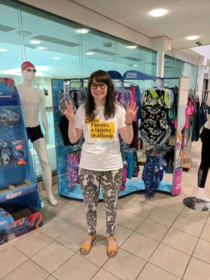Woman wearing Cystic Fibrosis t-shirt smiles outside a shop front