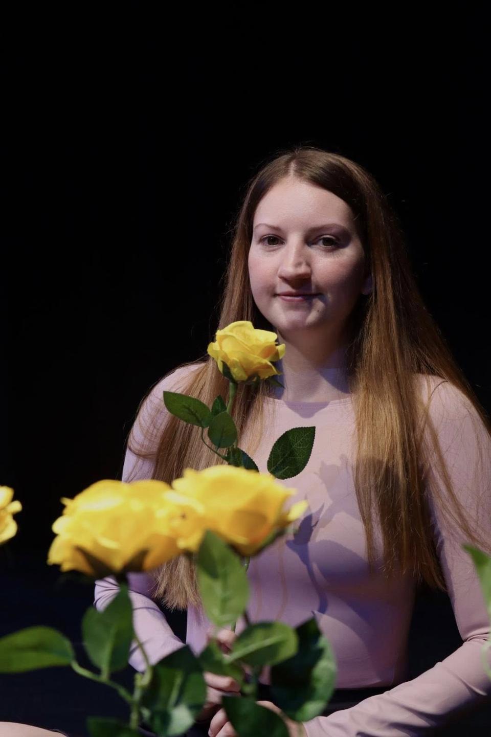 Caitlin stands behind yellow roses