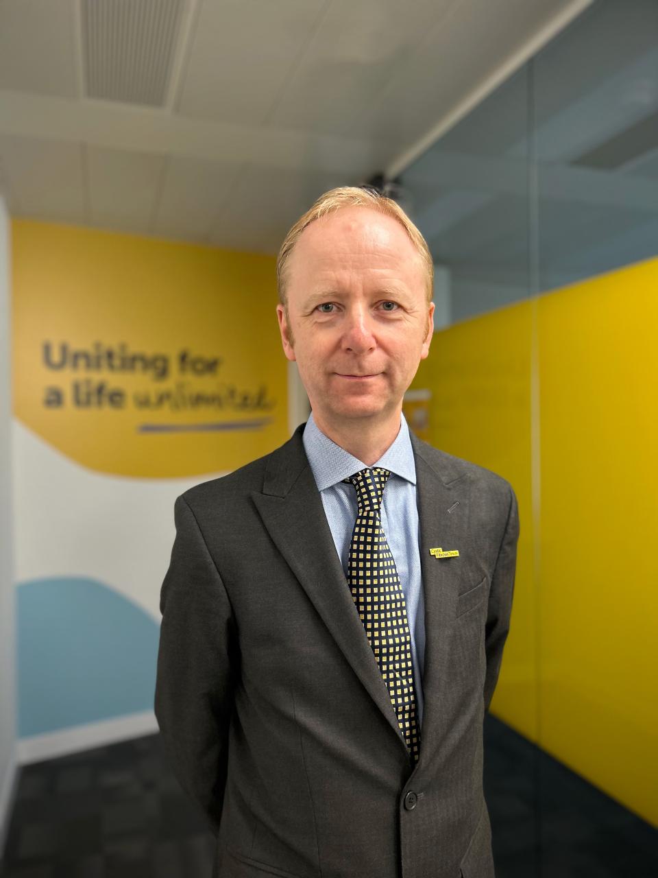 David Ramsden, Cystic Fibrosis Trust CEO stands in front of a sign reading "uniting for a life unlimited"