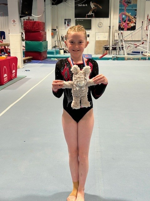 Kate at gymnastics. She holds a toy donkey in front of her and is wearing a medal