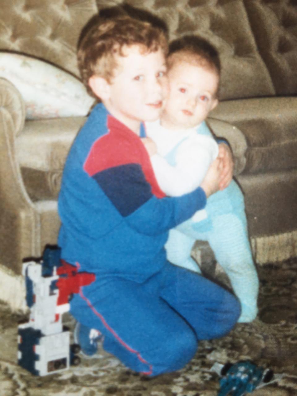 Mark is a bit older, crouched on the floor, holding his baby brother
