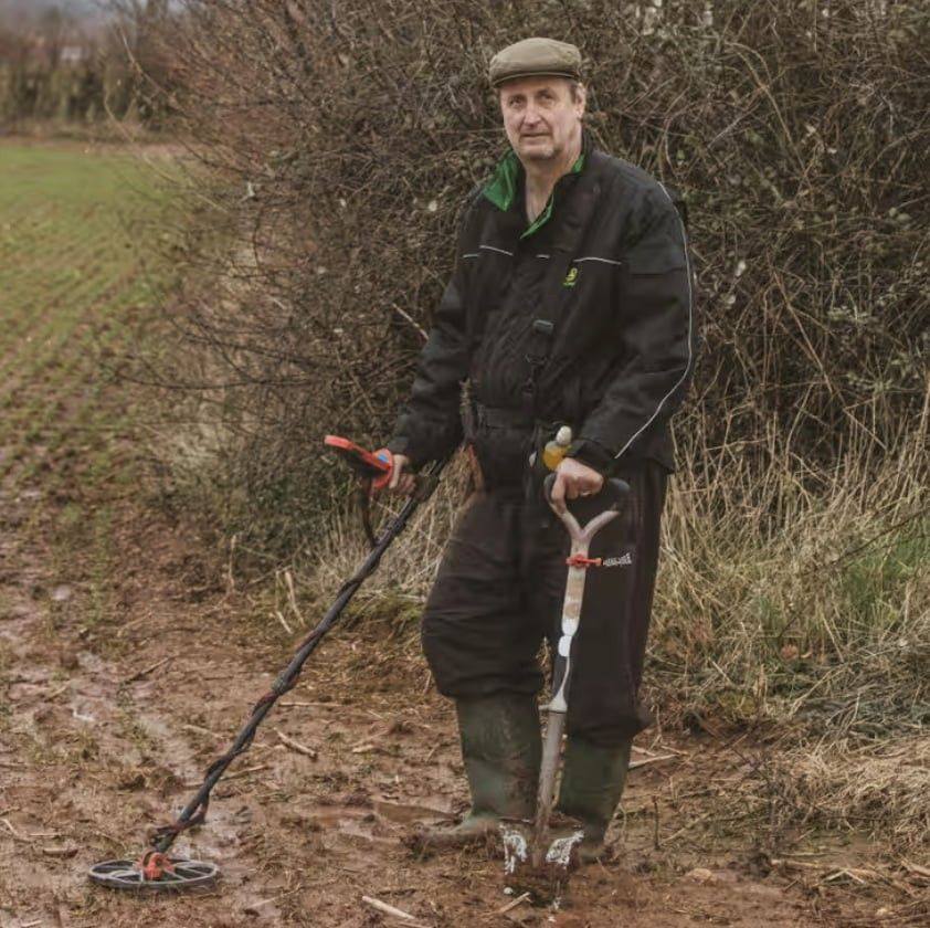 Morley stands in a field with a metal detector