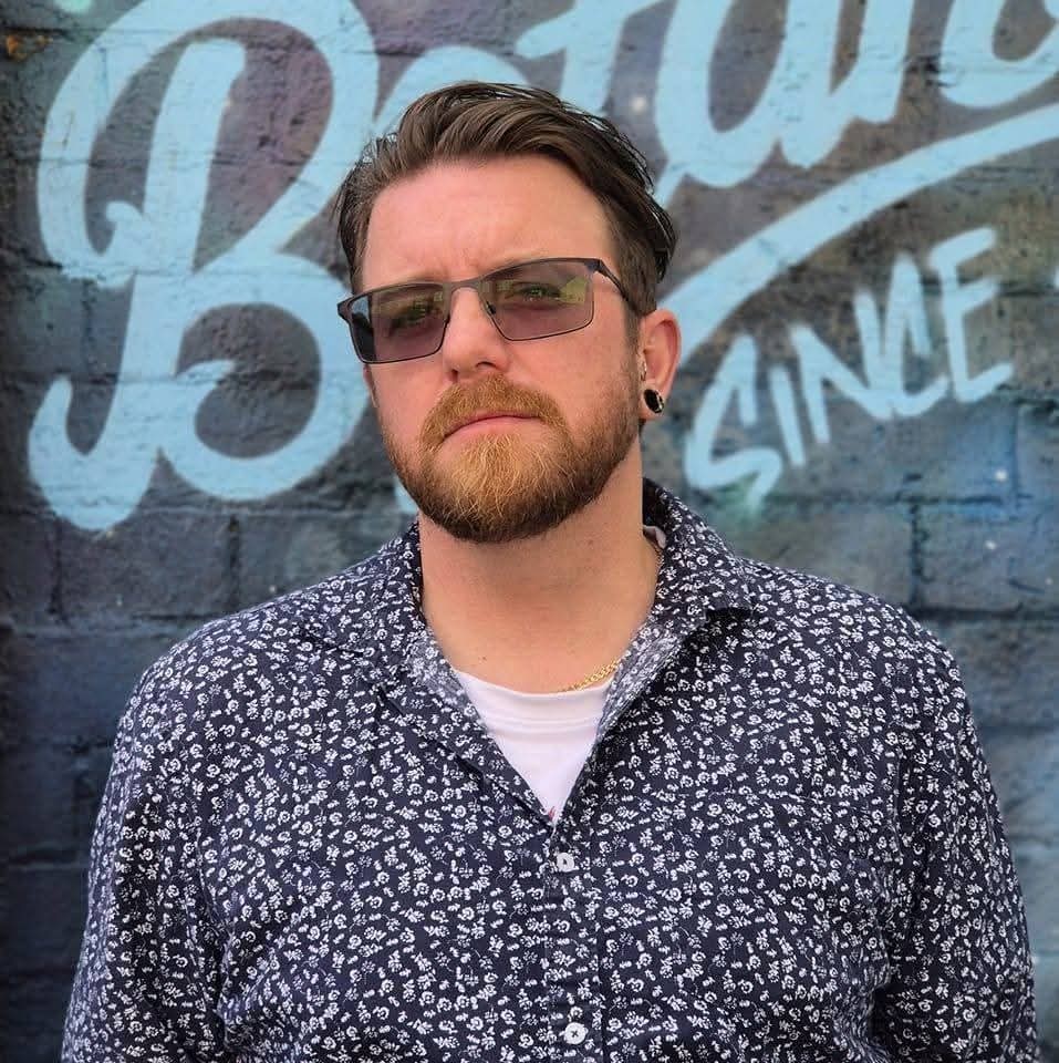 Adam wears sunglasses and looks into the camera