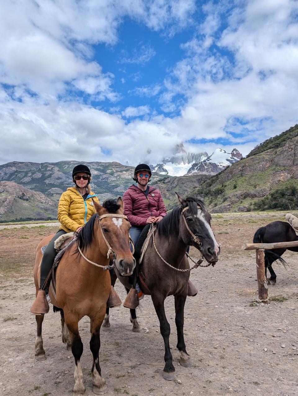 Josh and his wife sit on the back of horses surrounded by mountains
