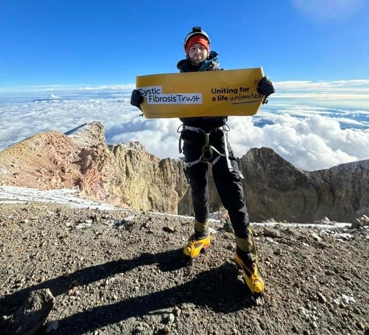 Kieran standing at top of a mountain holding a banner