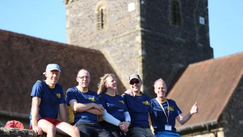 Five smiling adults sitting on a wall outside a church
