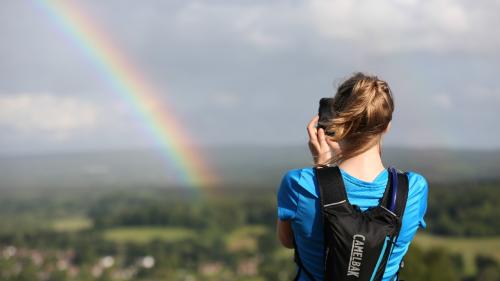 Young woman taking a photo of a rainbow and countryside