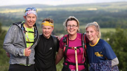 Four adults standing together with a countryside view behind them