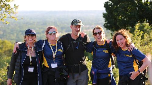 Five smiling adults standing together with trees and a view behind them
