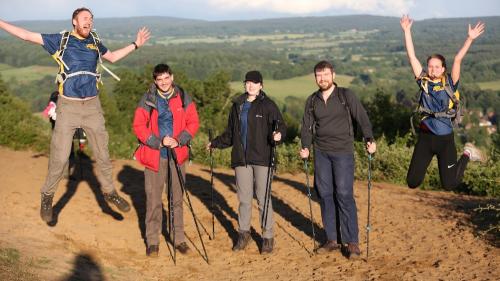 Five happy adults posing in walking gear with a countryside view behind them