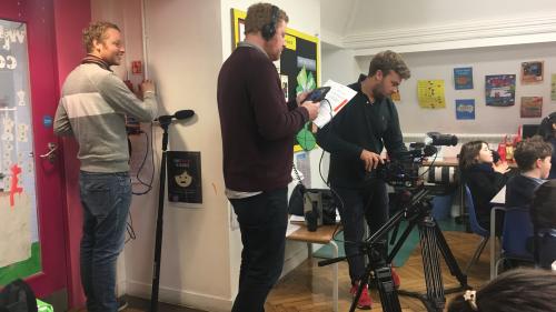 Three men with video recording equipment in the corner of classroom.