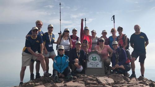 Big group of happy walkers standing with stone marker that says