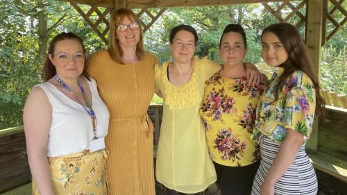 Five women all wearing yellow outfits in a wooden gazebo