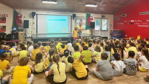 Group of primary aged school children listening to their friend in assembly. All wearing yellow.