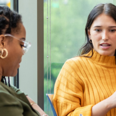 two women talking; one has a pen and clipboard to take notes