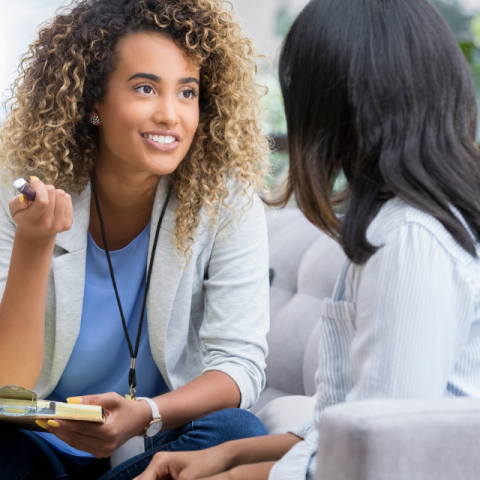 two women talking; one has a pen and clipboard to take notes