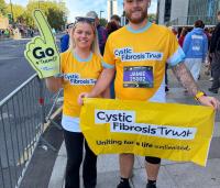a lady and a man wearing yellow cystic fibrosis tops, holding a yellow foam finger and yellow cystic fibrosis banner