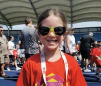 a young girl running a race, wearing a red top and sunglasses
