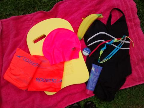 A black swimming costume and swim accessories on a pink towel