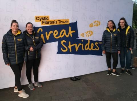 Four women in matching puffer jackets standing in front of a banner that says Great Strides
