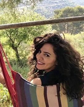 A light-skinned woman with dark brown hair sitting in a hammock looks over her shoulder and smiles at the camera.