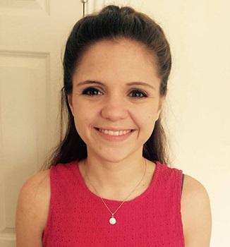 A young white woman with brown hair wearing a sleeveless pink top smiles at the camera