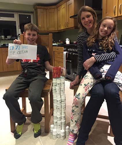 An image of a woman and two children, a boy and a girl, sitting on chairs next to a table made out of Creon pots.