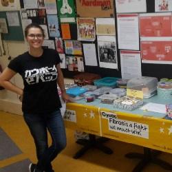 Two women with blonde hair standing in front of a table with cakes on it. Both women are holding a yellow balloon with 'Cystic Fibrosis no party' written on it.