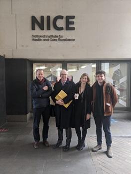 Four people standing outside of a building with NICE - National Institute for Health and Care Excellence - written on it