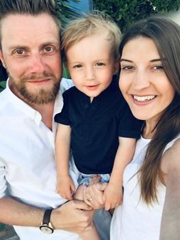 A white man with fair hair and beard and a white woman with brown hair smile with a young white boy with blonde hair.