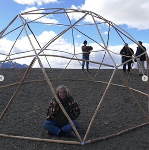 A girl sits inside a dome made out of wooden sticks
