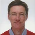 Man with dark brown hair, glasses, wearing blue collared shirt underneath red v jumper