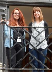 Two white women standing on a balcony smiling at the camera