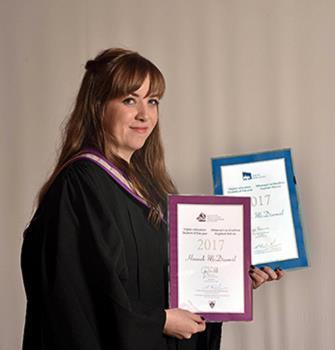 A woman with long fair hair wearing black graduation robes, holding two certificates and smiling at the camera.