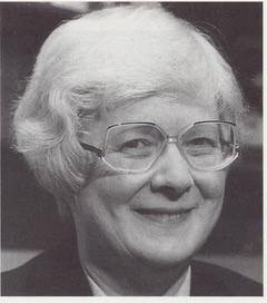 old woman with white hair and brown glasses wearing raincoat background of countryside