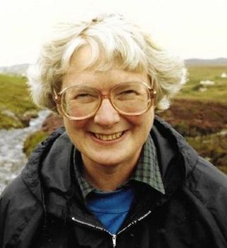 old woman with white hair and brown glasses wearing raincoat background of countryside