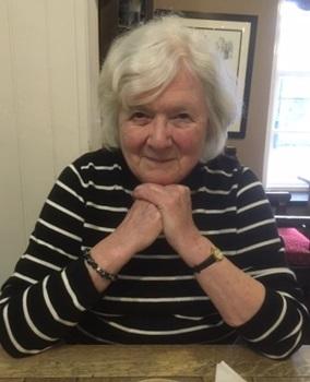 woman with white short hair wearing black top with white strips holding hands under chin looking at camera