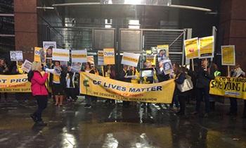 A group of people protest on a dark, rainy street. They are holding banners and placards about cystic fibrosis. A large banner is at the front of the group, and it says 'CF lives matter'.