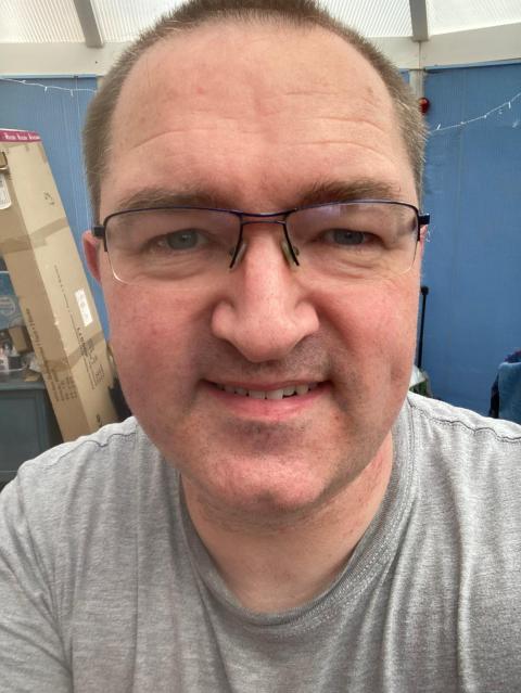 Man with shaved head, wearing glasses and grey t-shirt