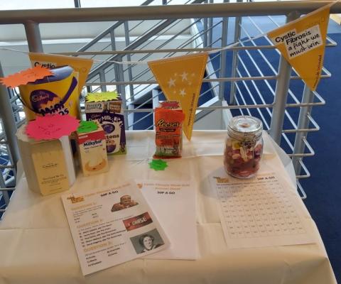 Company fundraising table, with Cystic Fibrosis Trust banner hanging on railing behind table