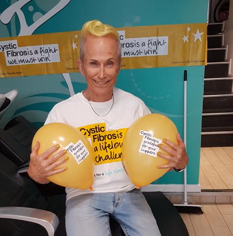 Man with yellow dyed hair holding two yellow Cystic Fibrosis Trust balloons where CF Trust t-shirt