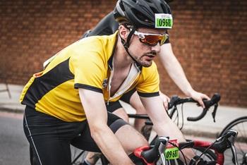 man on bike wearing yellow cycling jersey with black stripe, black helmet on red and black racing bike