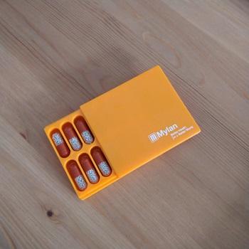 small orange box partly open with red and white medication inside in pill-shaped compartments 