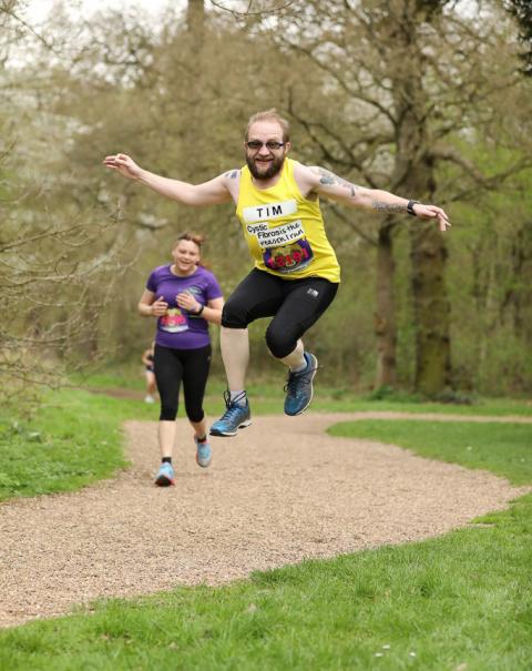 A man with a beard in a yellow running vest jumps into the air.