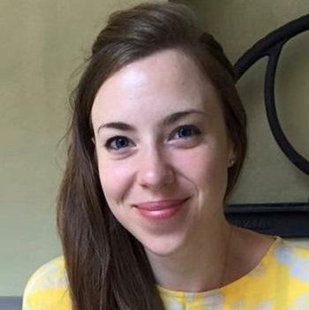 woman with long brown hair smiling wearing yellow shirt with white patterns 