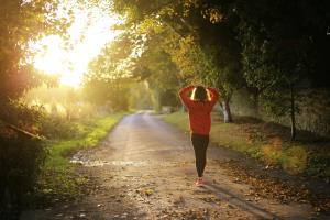 A woman taking a breather from exercising, standing on a country lane looking at the sun